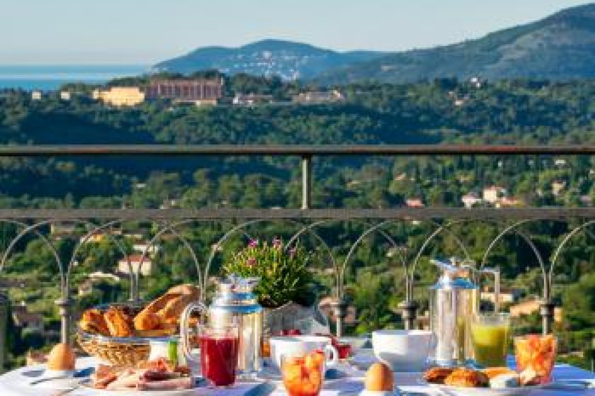 Breakfast table set on a terrace with bread, jam, eggs and juice, overlooking hills and distant coastline