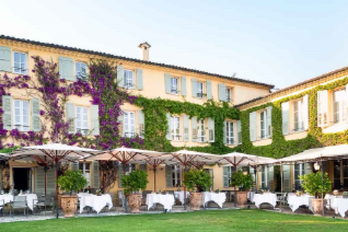 Hotel façade with bougainvillea and ivy, terrace tables with umbrellas on lawn