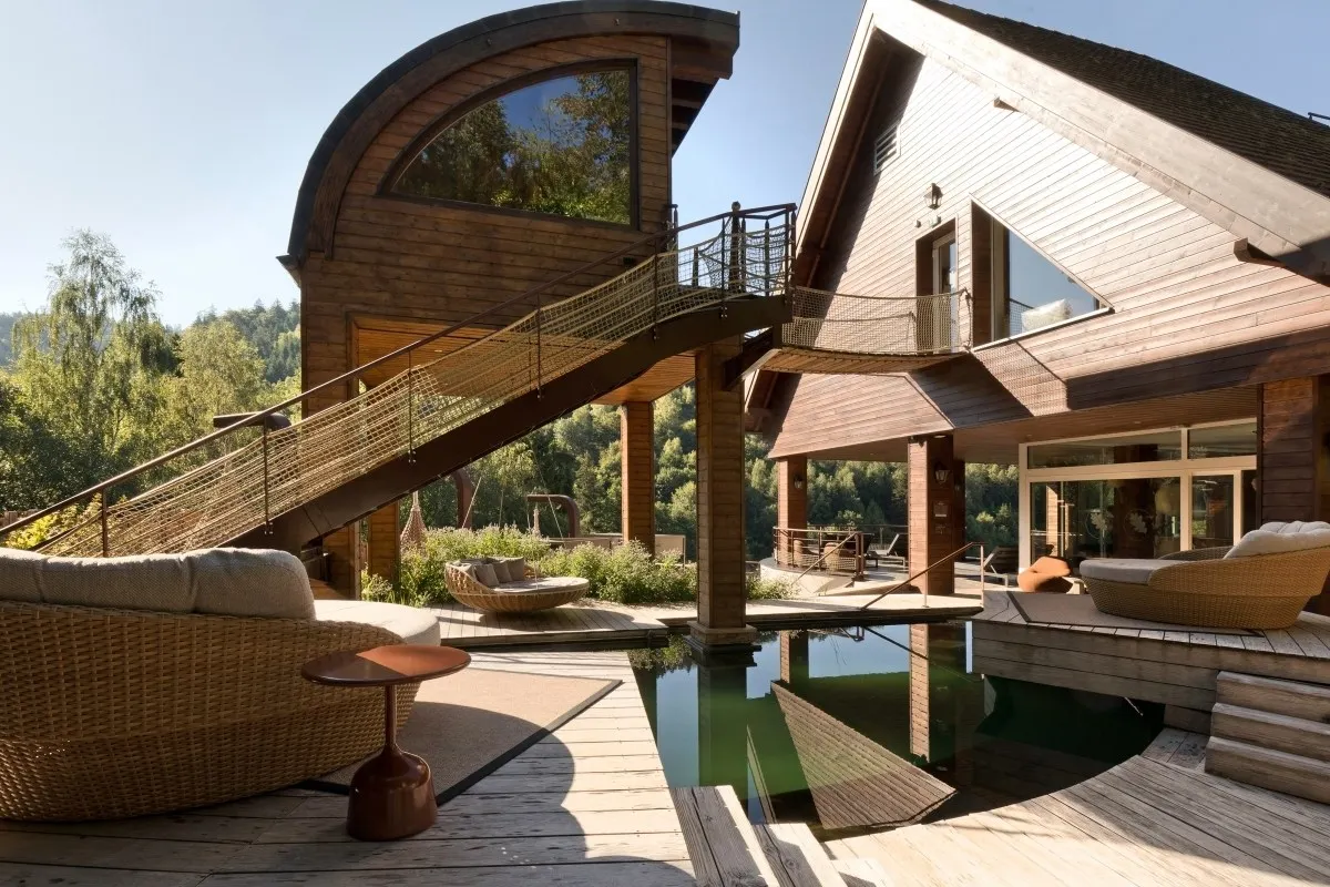 Modern wooden hotel exterior with elevated walkway, pool, and lounge terrace surrounded by trees