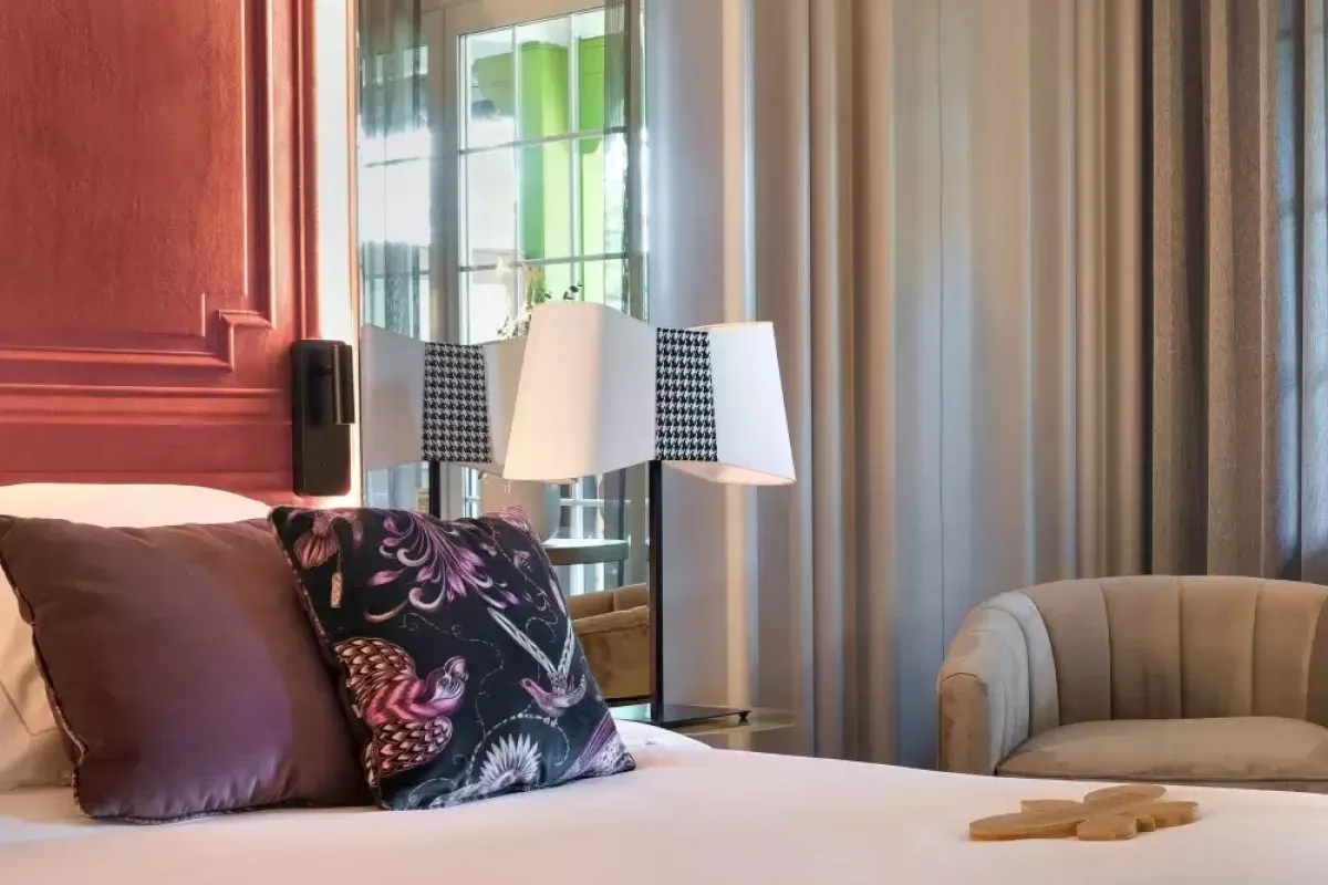 Guest room bed with patterned cushions, red paneled headboard and modern table lamp