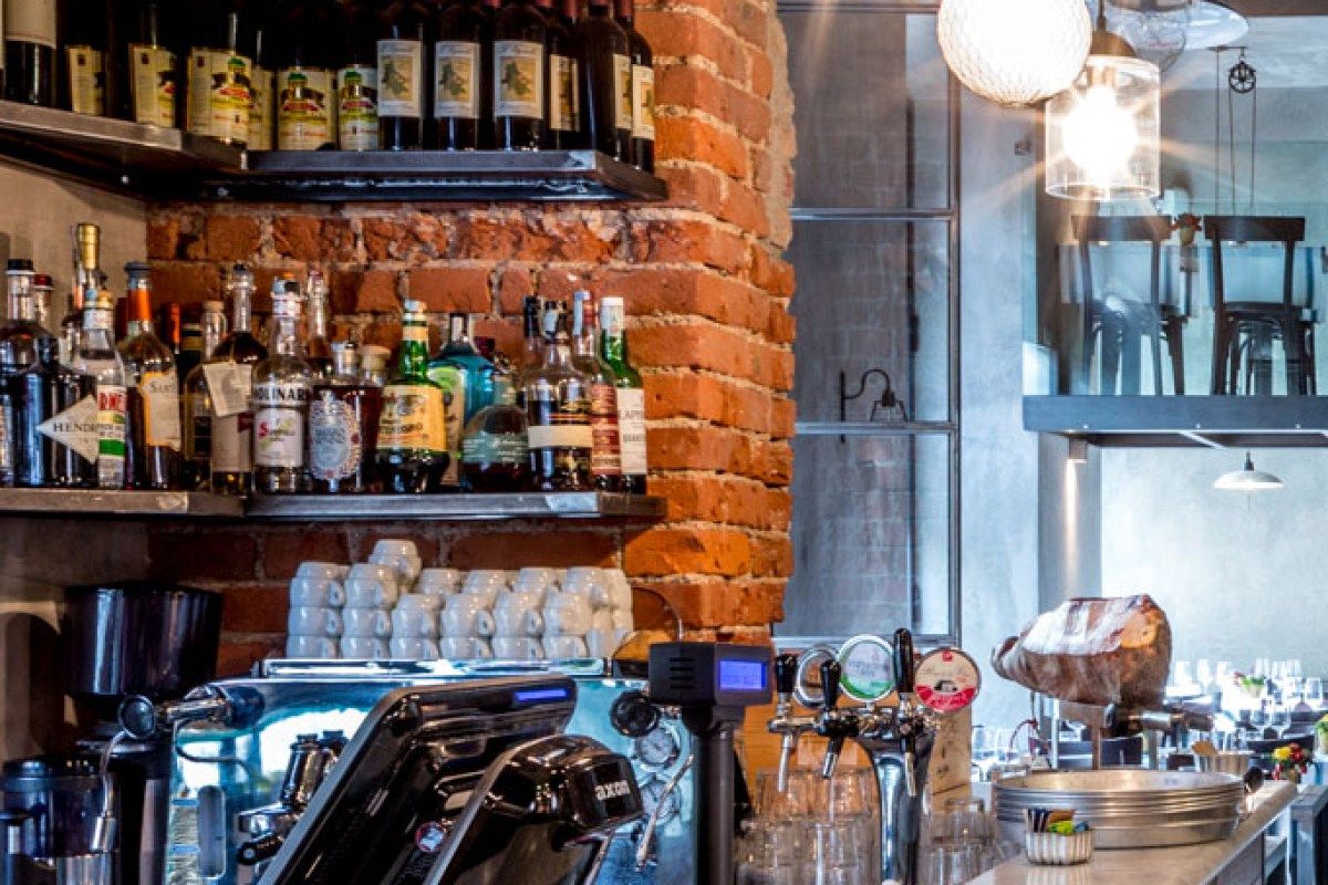 Interior bar area with brick column, bottles, tap and dining chairs visible beyond