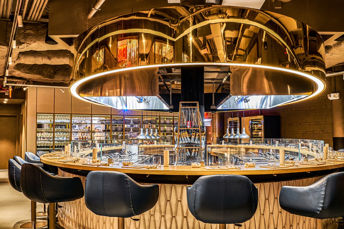 Oval-shaped dining counter with bar stools under a large round mirrored light fixture, open kitchen behind