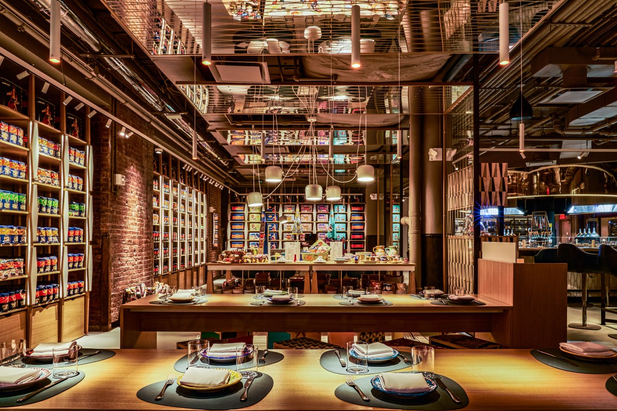 Restaurant dining room with wood tables set for dining, shelves of Italian pasta and snack products along brick wall