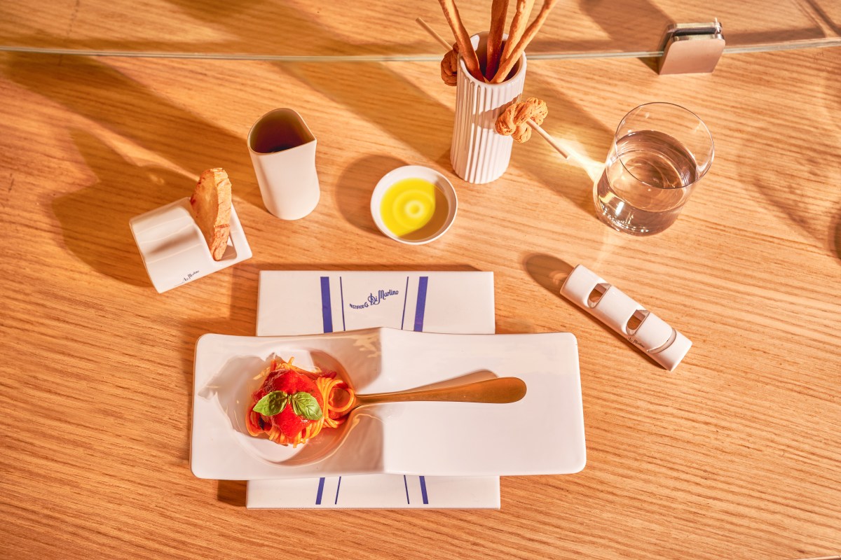 Overhead shot of a spaghetti pomodoro dish with basil on white plates, bread sticks and water glass on wood table