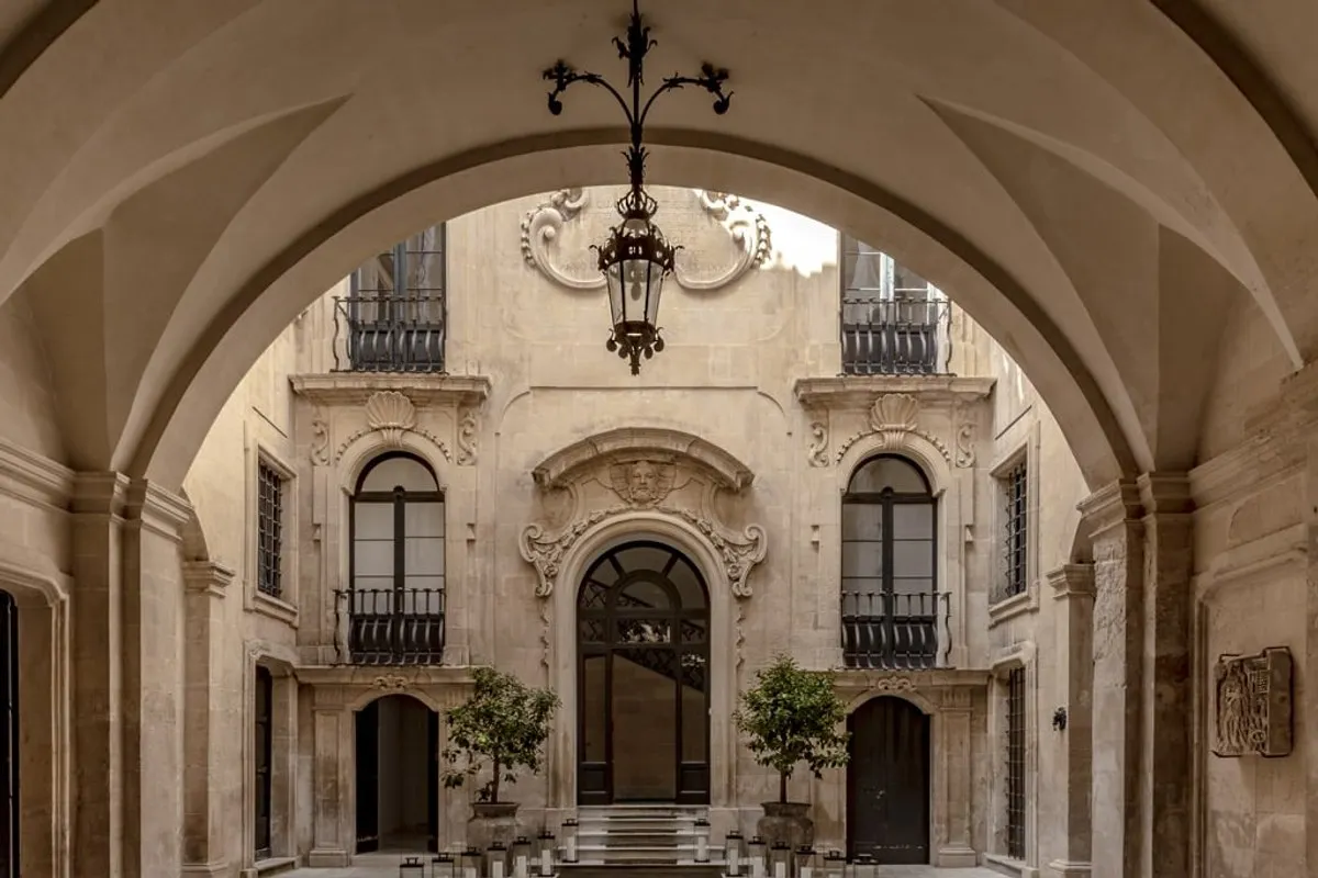 Elegant stone courtyard of the palazzo seen through an arched passage, with balconies, carved details and a hanging lantern