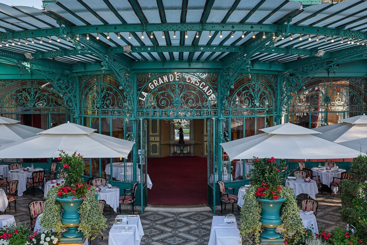 Wide view of the restaurant's terrace with set tables, umbrellas, flowers and ornate entrance.