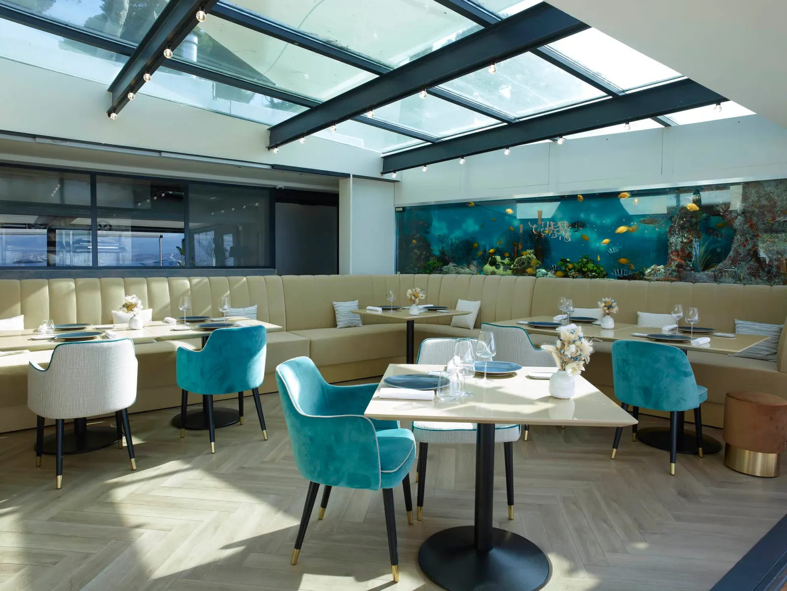 The dining room of La Maison de Bacon on Cap d'Antibes, with a glass roof, velvet chairs, banquettes and a long aquarium wall