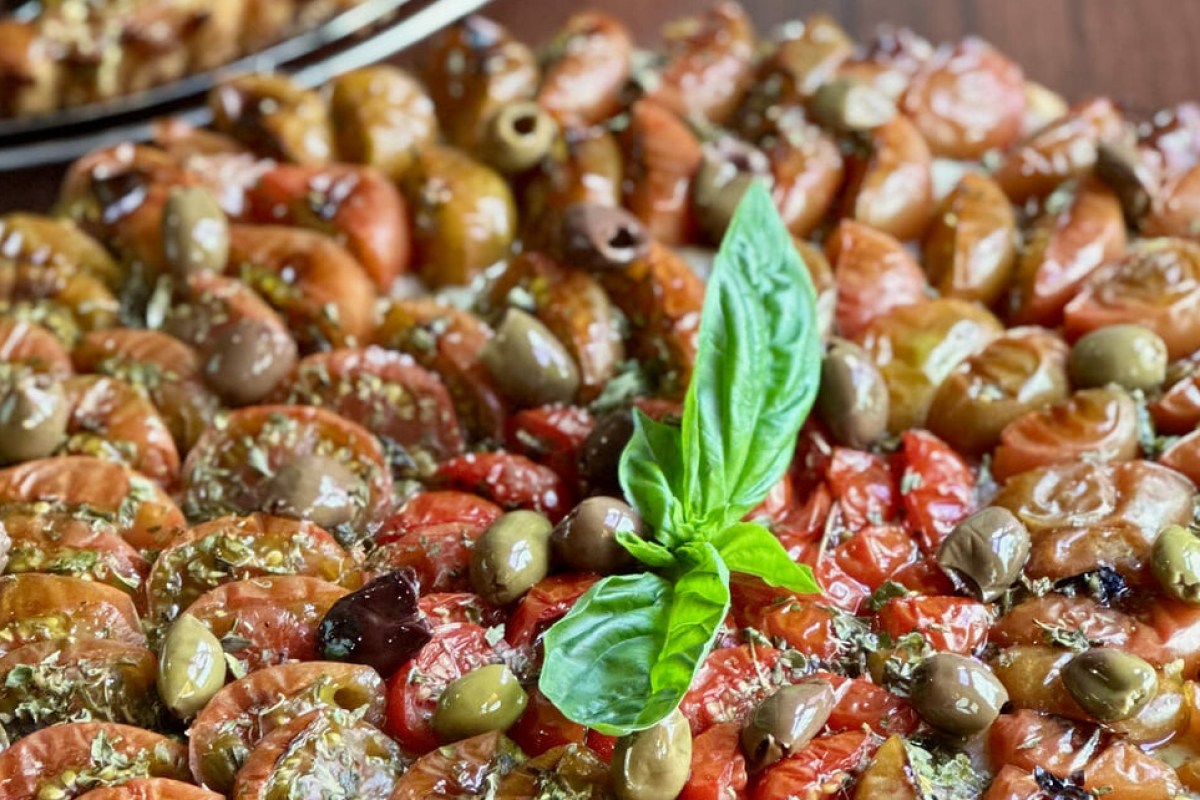 Close-up of a tomato and olive salad topped with a fresh basil leaf, glistening with olive oil and herbs.