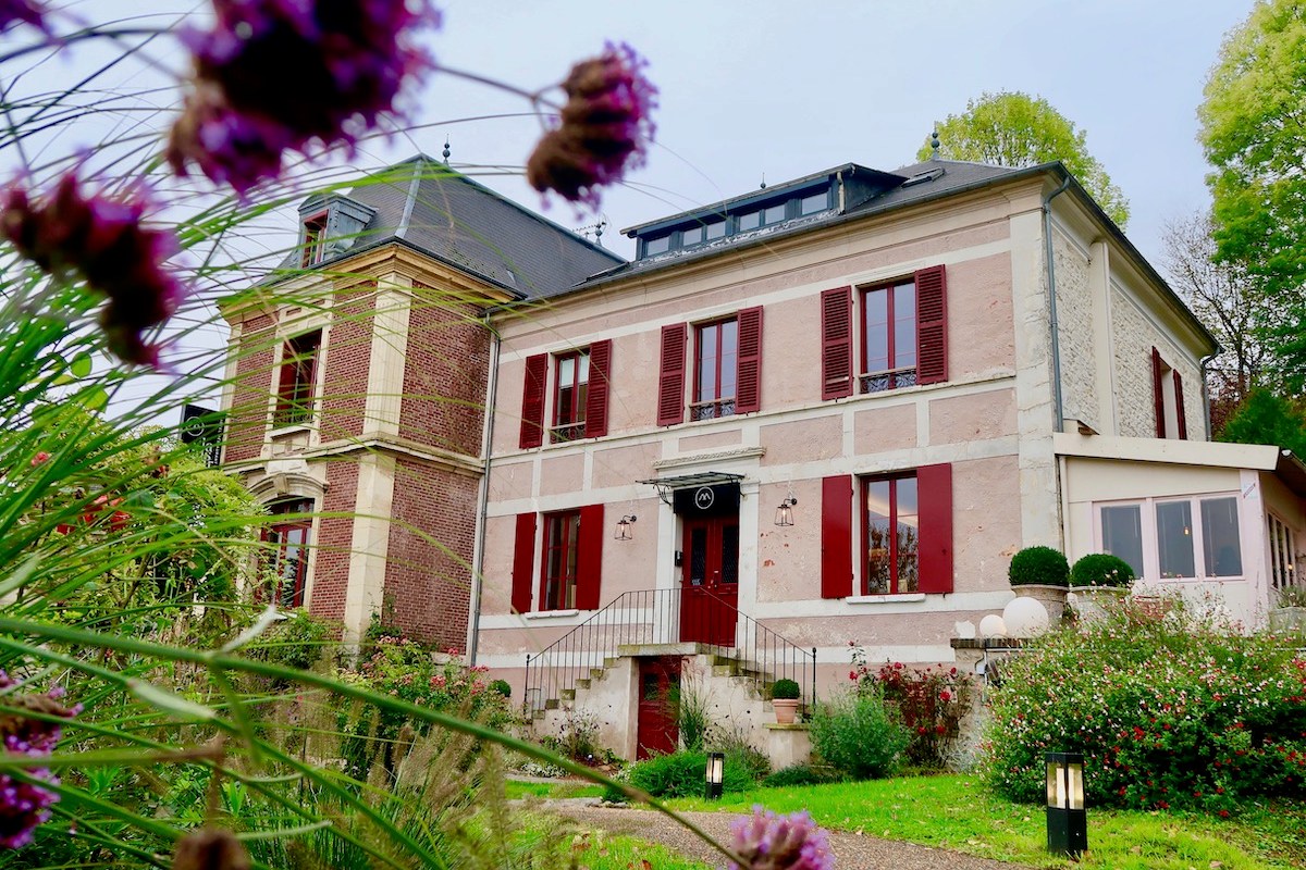 La Musardière exterior facade with red shutters, terrace and garden, framed by purple flowers