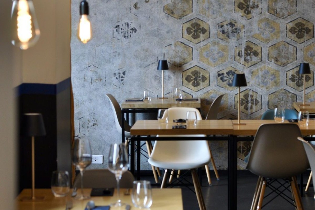 Modern restaurant dining room interior with patterned wallpaper, wooden tables and pendant lights