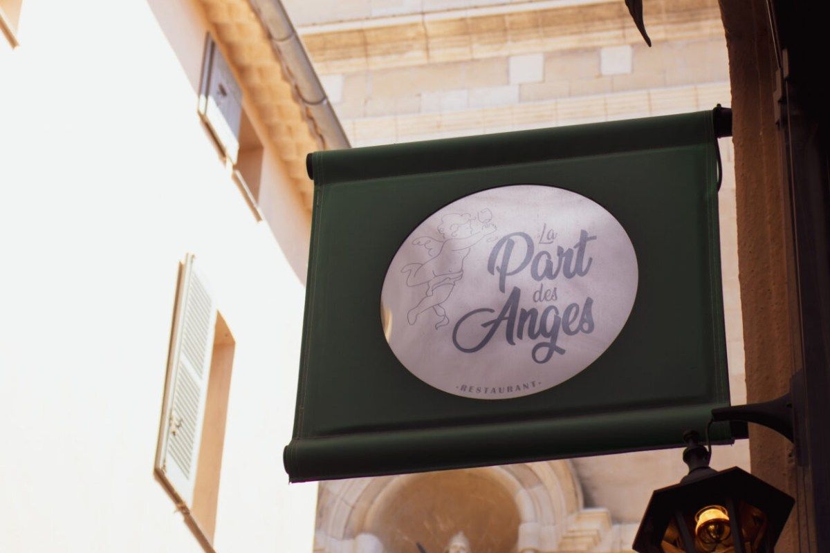 Restaurant sign reading 'La Part des Anges' hanging outside a stone building entrance