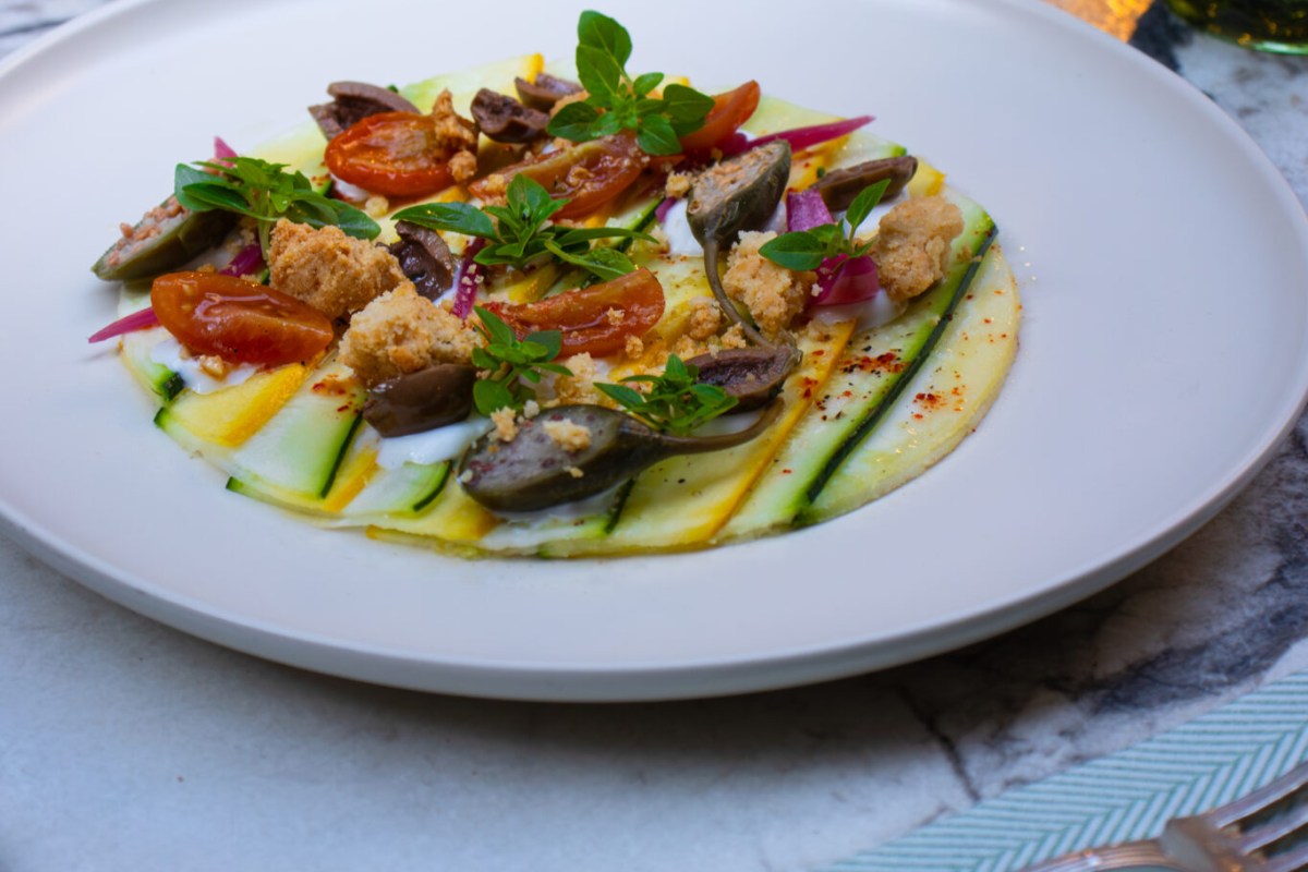Plate with zucchini ribbon carpaccio, cherry tomatoes, olives and herbs