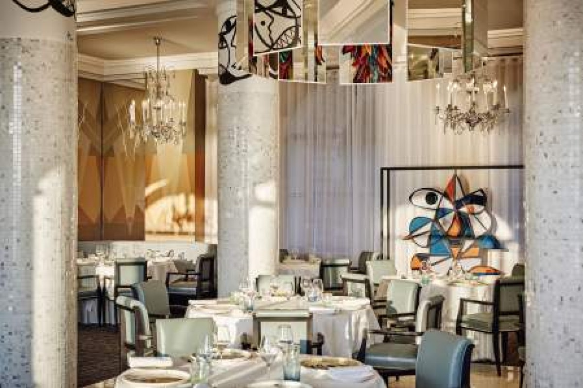 Elegant dining room with mosaic columns, chandeliers, colorful art and tables set for dining