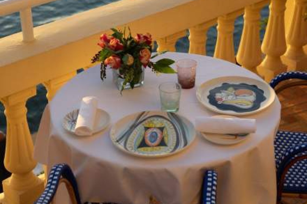 Round table set for two on a yellow-balustraded terrace overlooking the sea at sunset