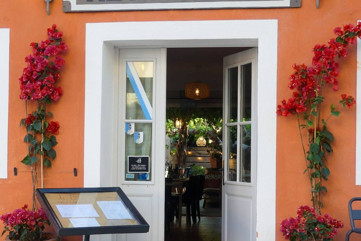 Restaurant entrance with orange facade, flowering bougainvillea, open door showing terrace and menu board outside