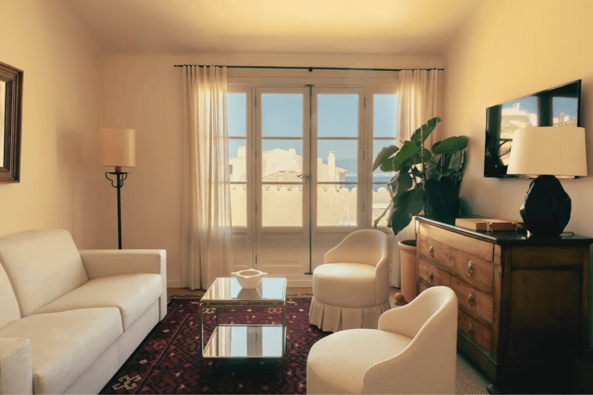 Guest suite living area with cream sofa, armchairs, antique dresser and French doors opening to a view