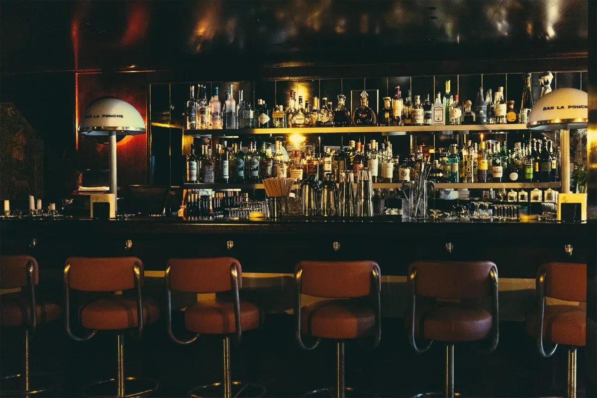 Dimly lit hotel bar with leather stools, shelves of liquor bottles and lamps reading 'Bar La Ponche'