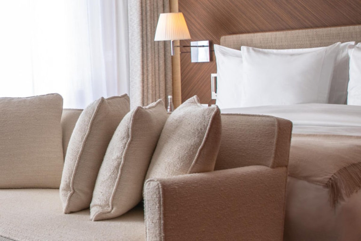 Hotel room with beige armchair, pillows and bed with wooden accents