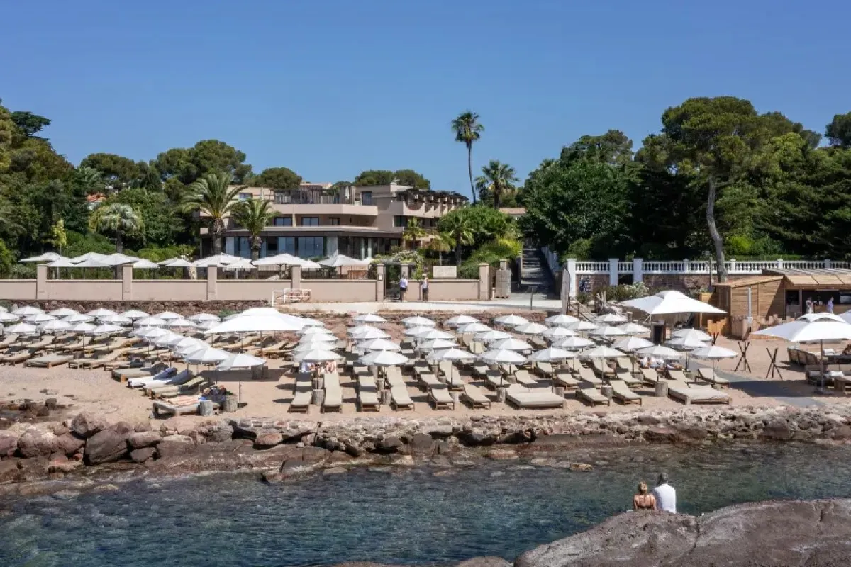 Modern hotel building seen from rocky shoreline with beach loungers and umbrellas in front