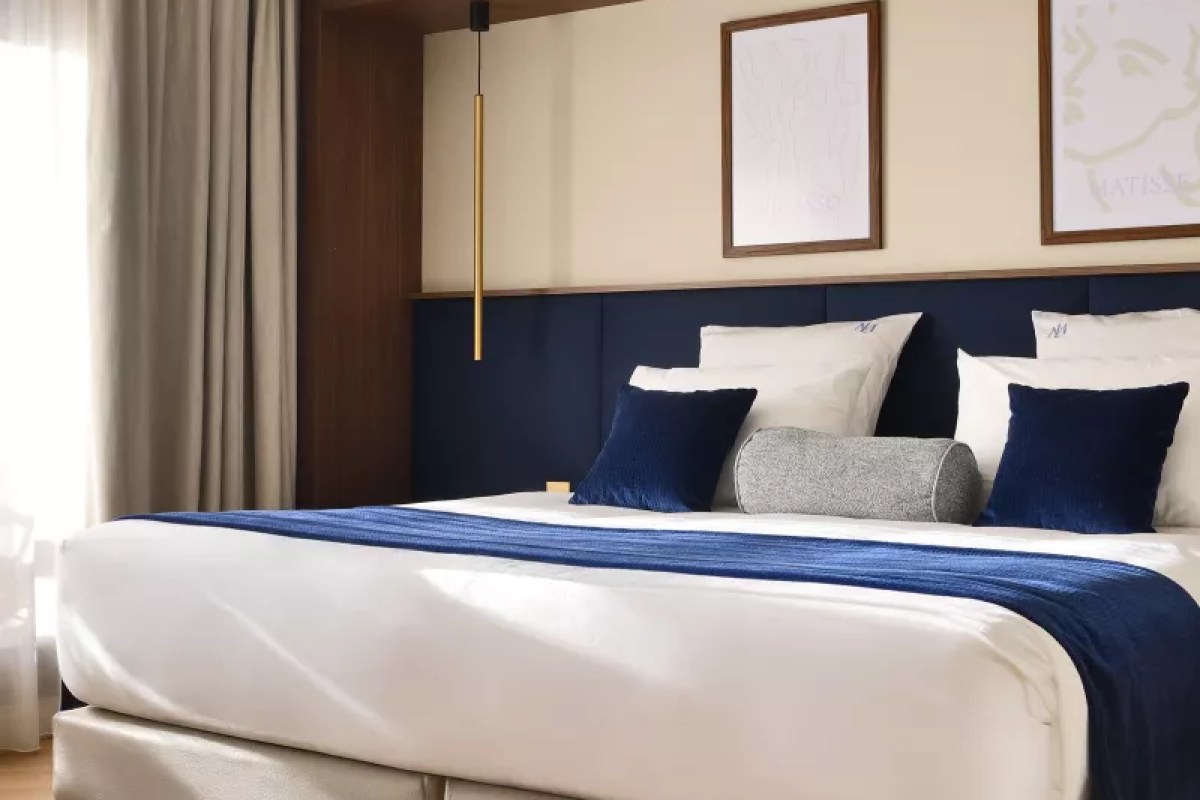 Hotel bedroom with navy blue headboard, white and blue bedding and framed art
