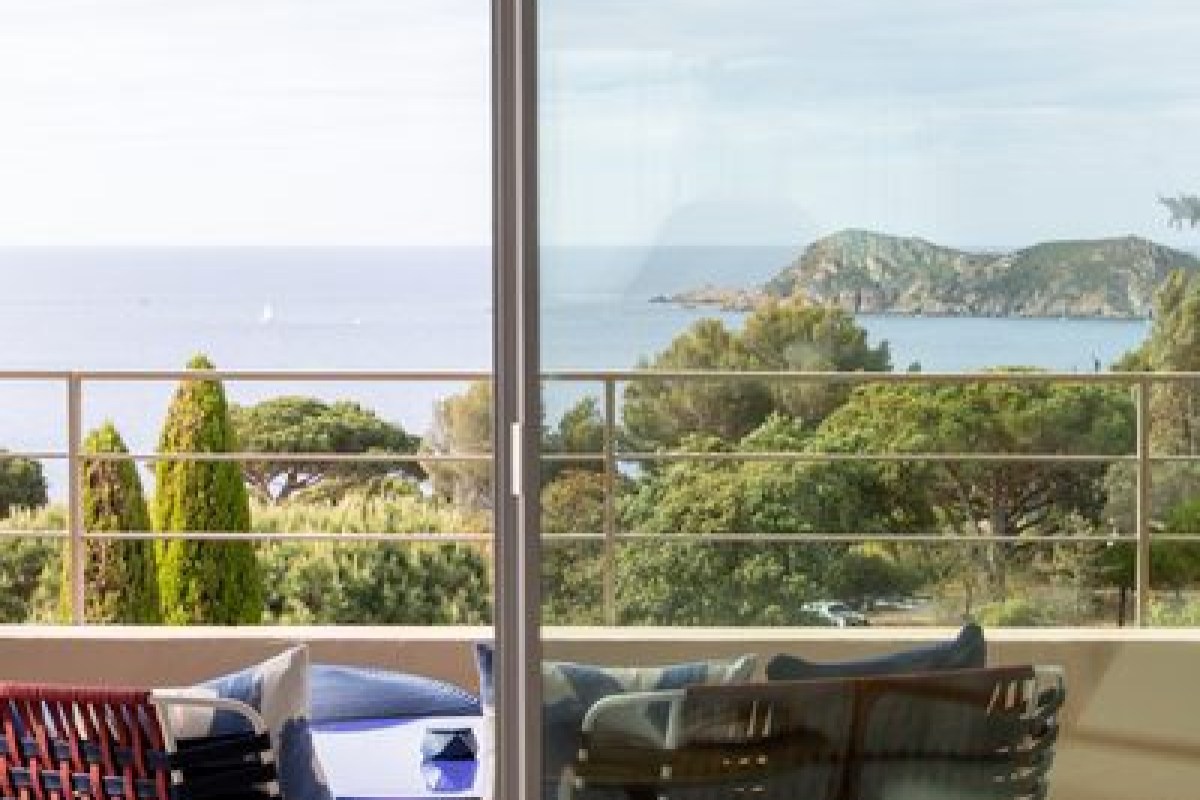 Balcony view through glass door showing sea, cliffs and greenery with lounge furniture