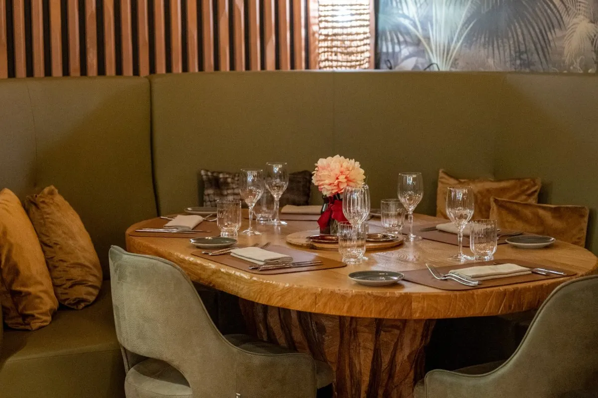 An elegant round dining table set with wine glasses, napkins, and a flower centerpiece in a plush booth