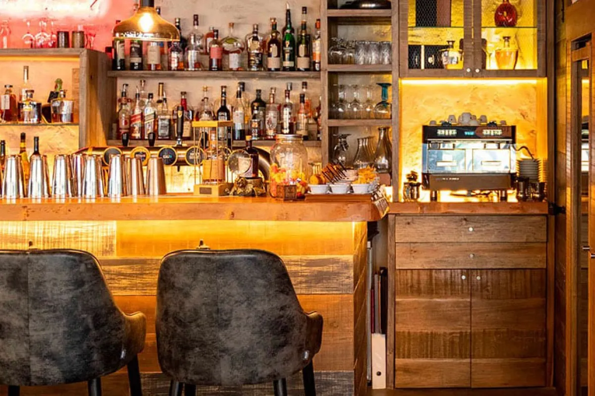 A well-stocked restaurant bar with shelves of liquor bottles, bar stools, and an espresso machine