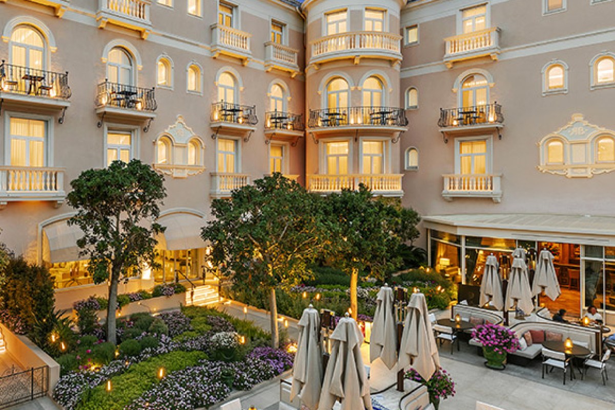 Hotel courtyard terrace at dusk with lounge seating, umbrellas, and warmly lit balconies overlooking greenery