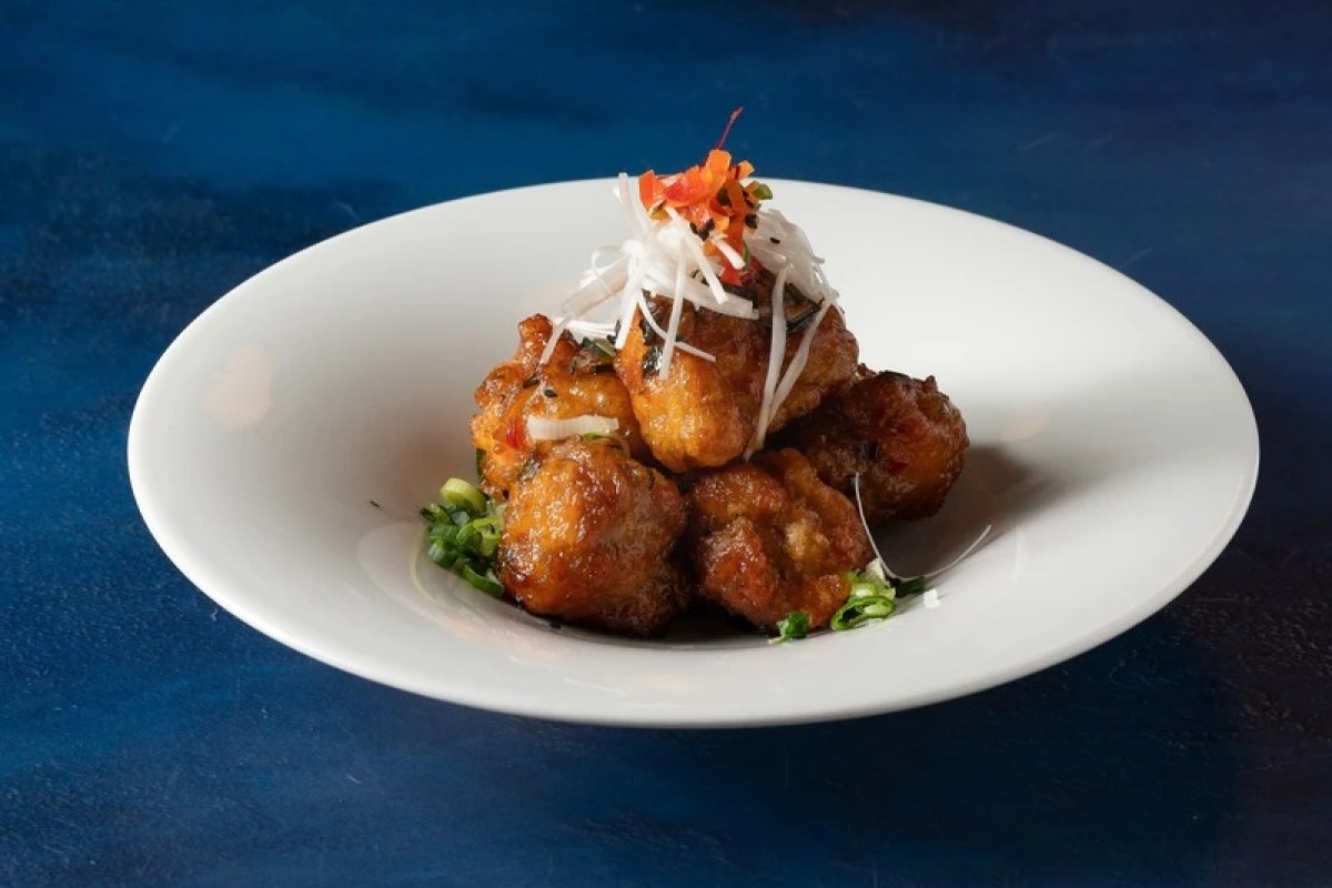 White plate of fried cauliflower bites topped with shredded daikon and chili on blue background