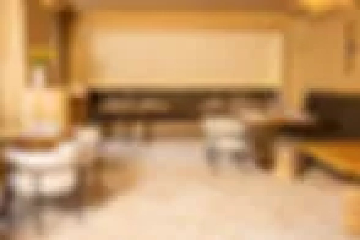 Blurry interior view of a dining room with pale walls, wooden furniture and white chairs