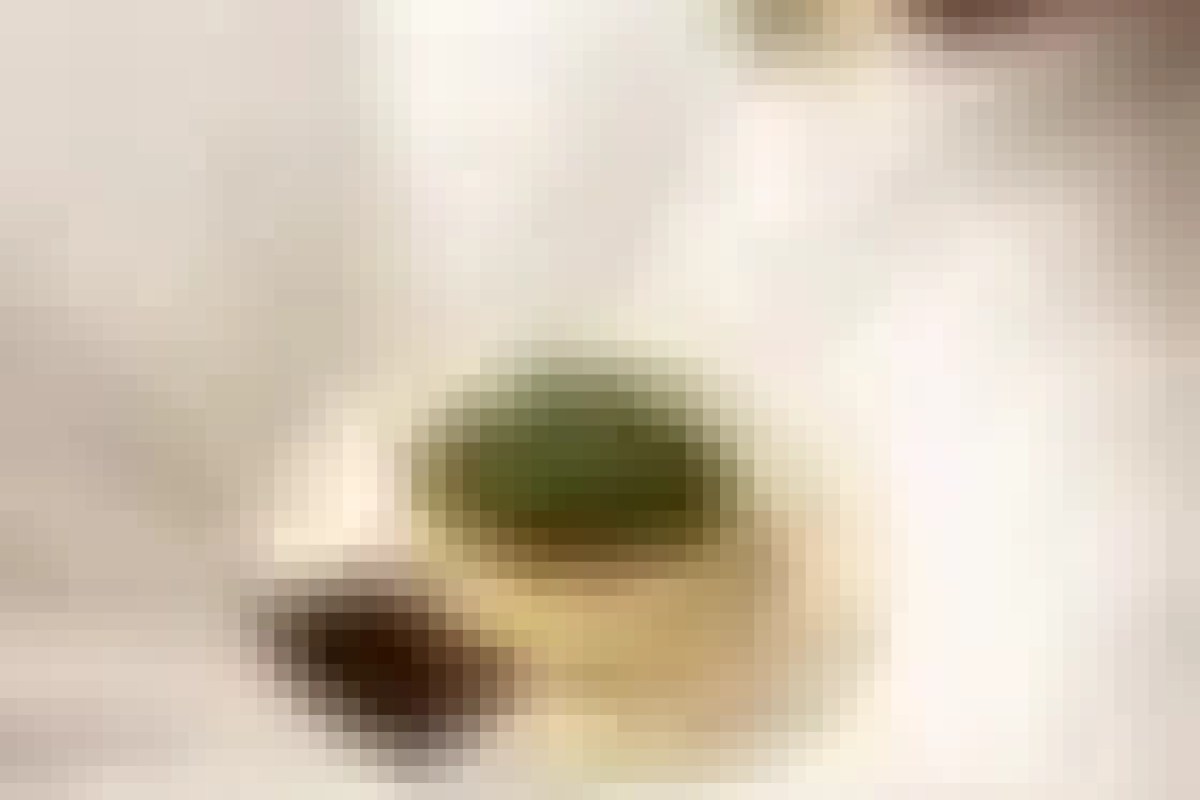 Blurry close-up of a plated dish with a round green item on a light tablecloth