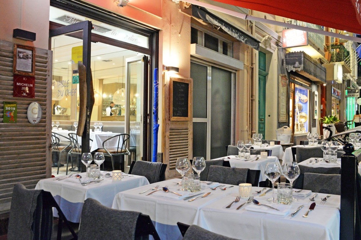 Exterior terrace of La Table du Chef at night, set tables with wine glasses and candles on a narrow Cannes street.