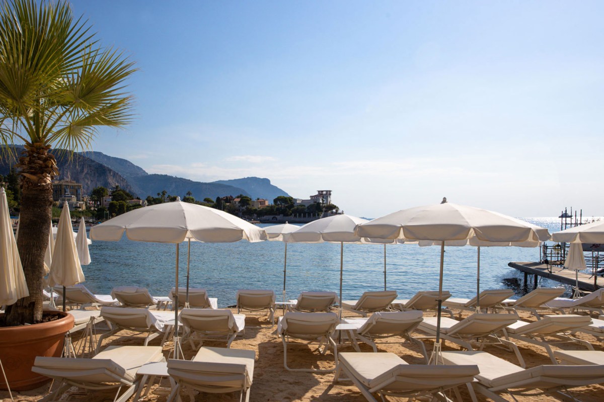 Beach club with white lounge chairs and umbrellas facing the sea, cliffs in background