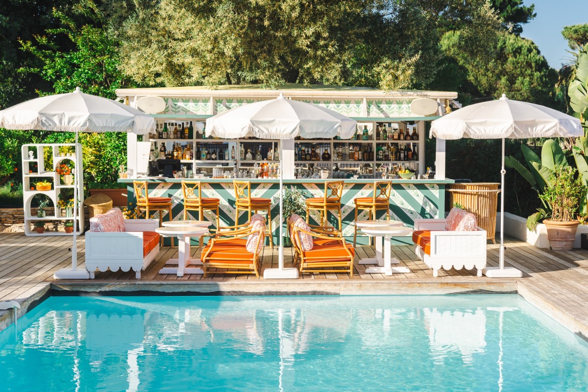 Poolside bar with striped awning, umbrellas, lounge seating and pool in foreground
