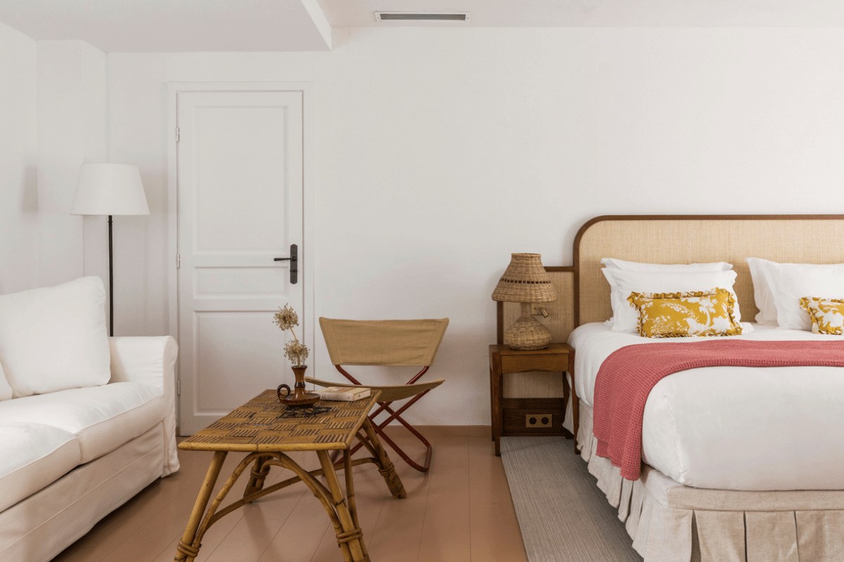 Bright guest room with woven cane headboard, white linens, armchair and sofa