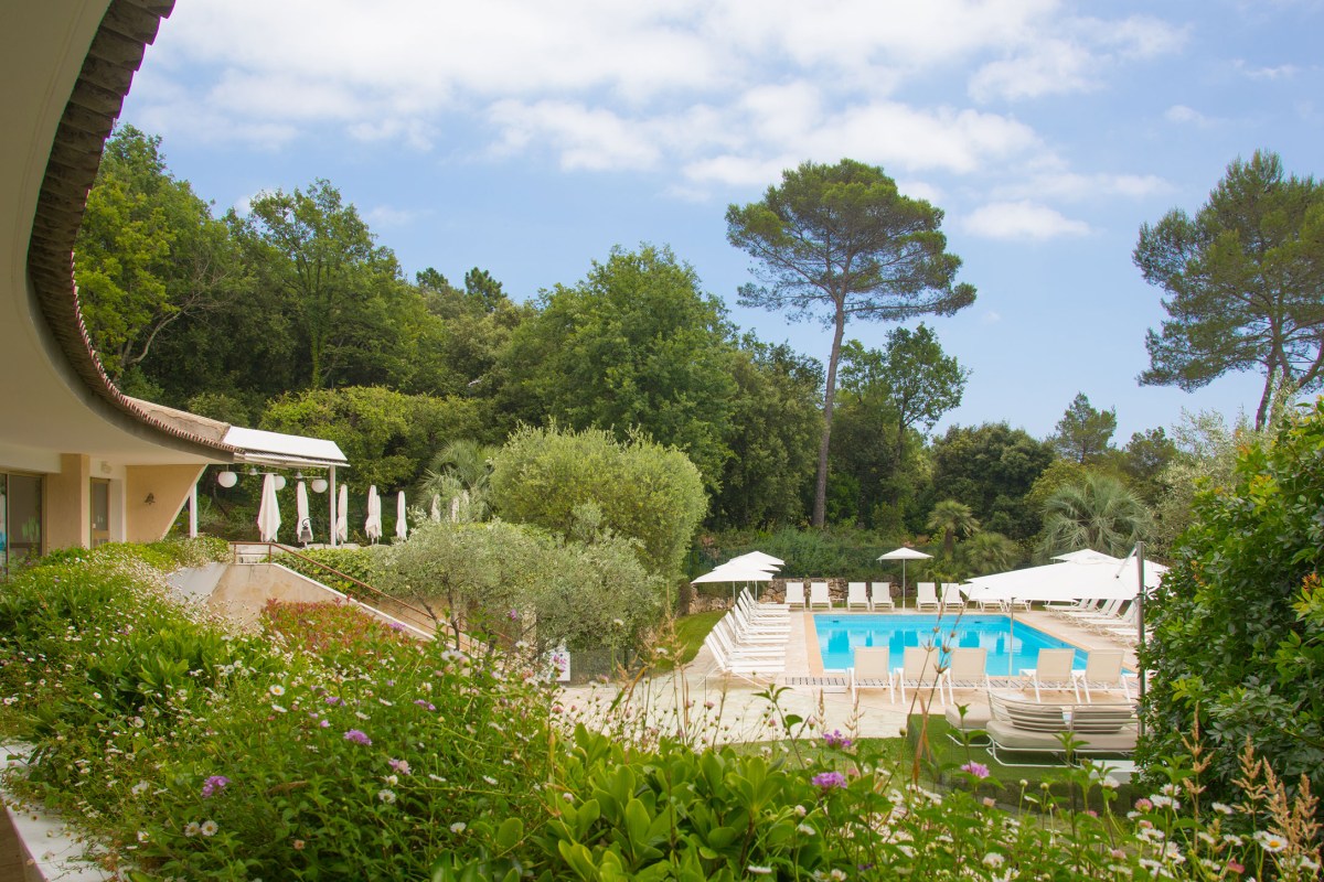 View of hotel's curved building exterior overlooking pool and garden with pine trees