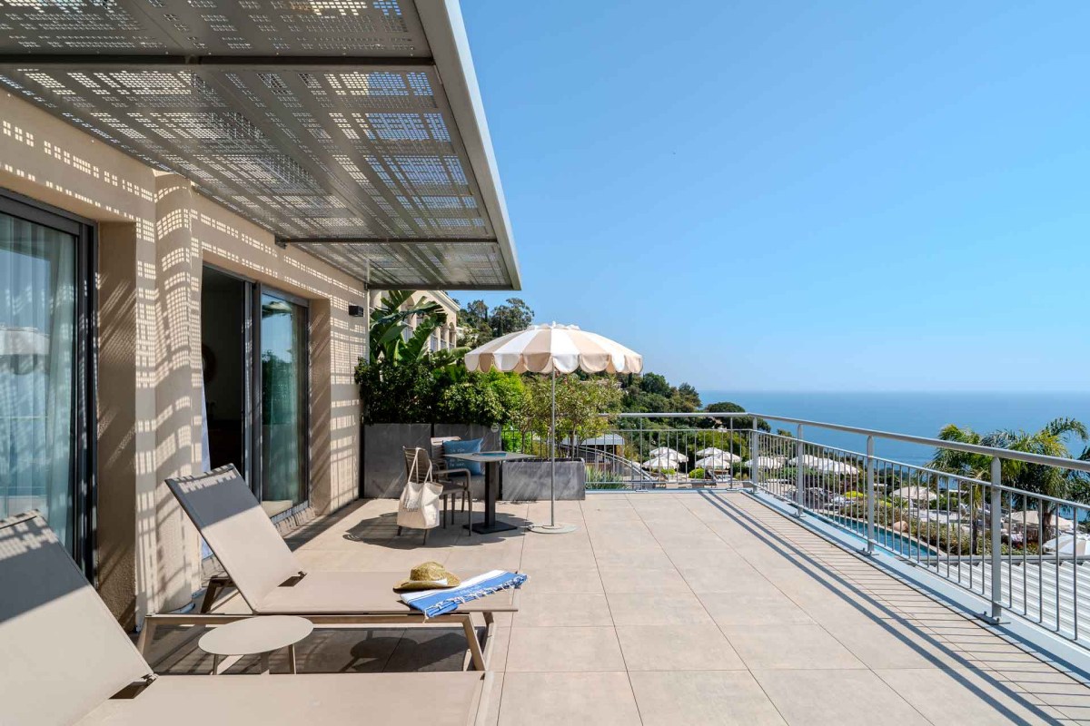Hotel terrace with lounge chairs, umbrella and sea view, pool visible below