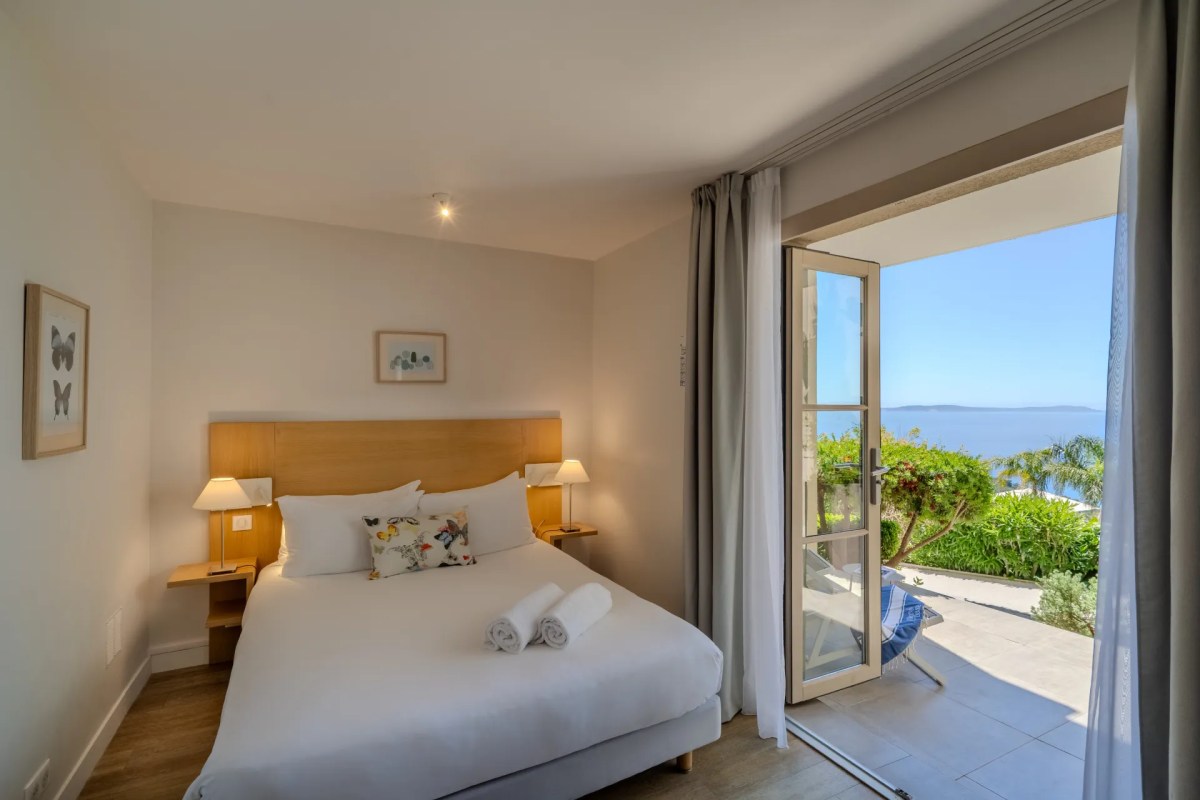 Bright guest room with white bed and open door to a sea-view balcony