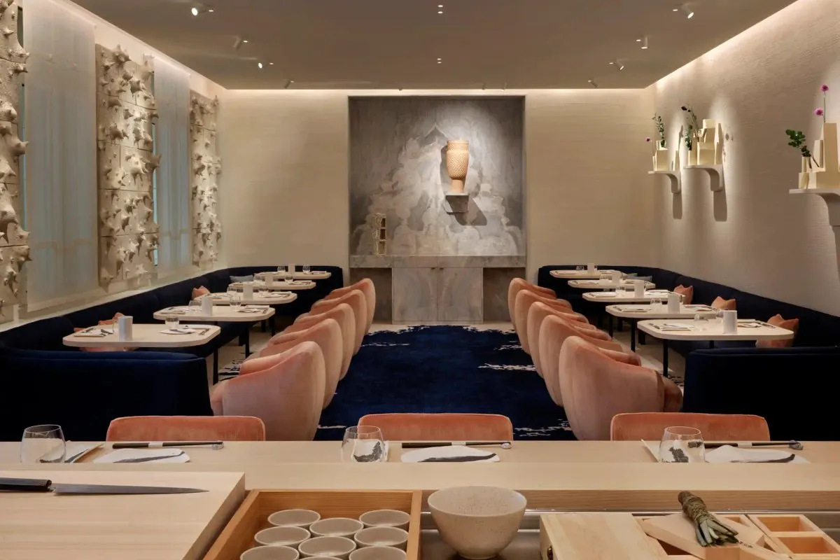 The dining room of L'Abysse Monte-Carlo seen from the light-wood sushi counter, with shell-pink chairs and navy banquettes