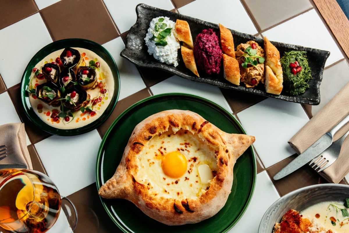 Overhead shot of Georgian dishes: khachapuri with egg, eggplant rolls, and mezze platter on tiled table