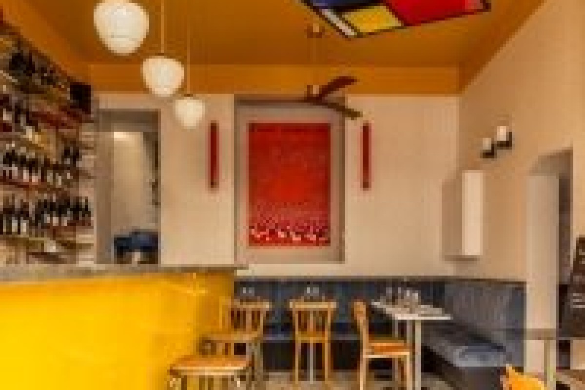 Colorful dining area at LAZU with yellow bar counter, wine bottles, pendant lights, and red artwork