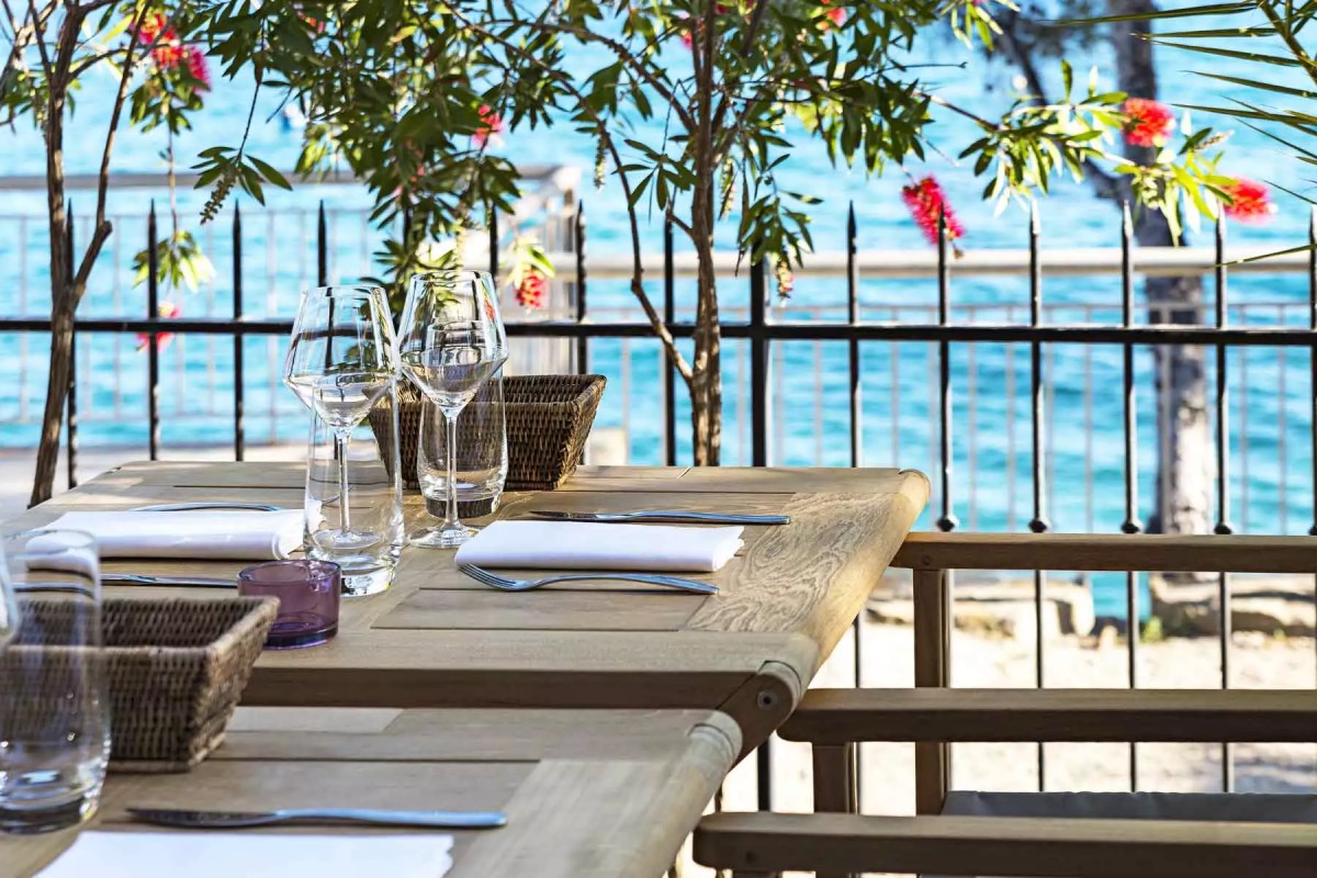 Outdoor restaurant table set with glasses and cutlery overlooking the sea