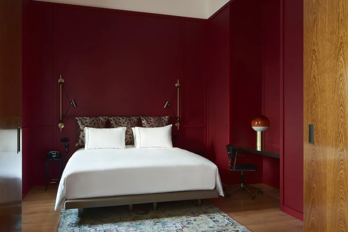 Deep red guest room with white bed, wooden wardrobe and desk area
