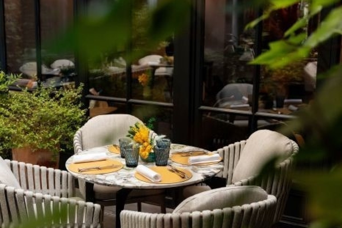 Outdoor terrace table set among greenery with view into restaurant interior