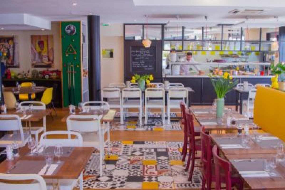 Bright dining room with patterned tile floor, red and white chairs, set tables and open kitchen with chefs.