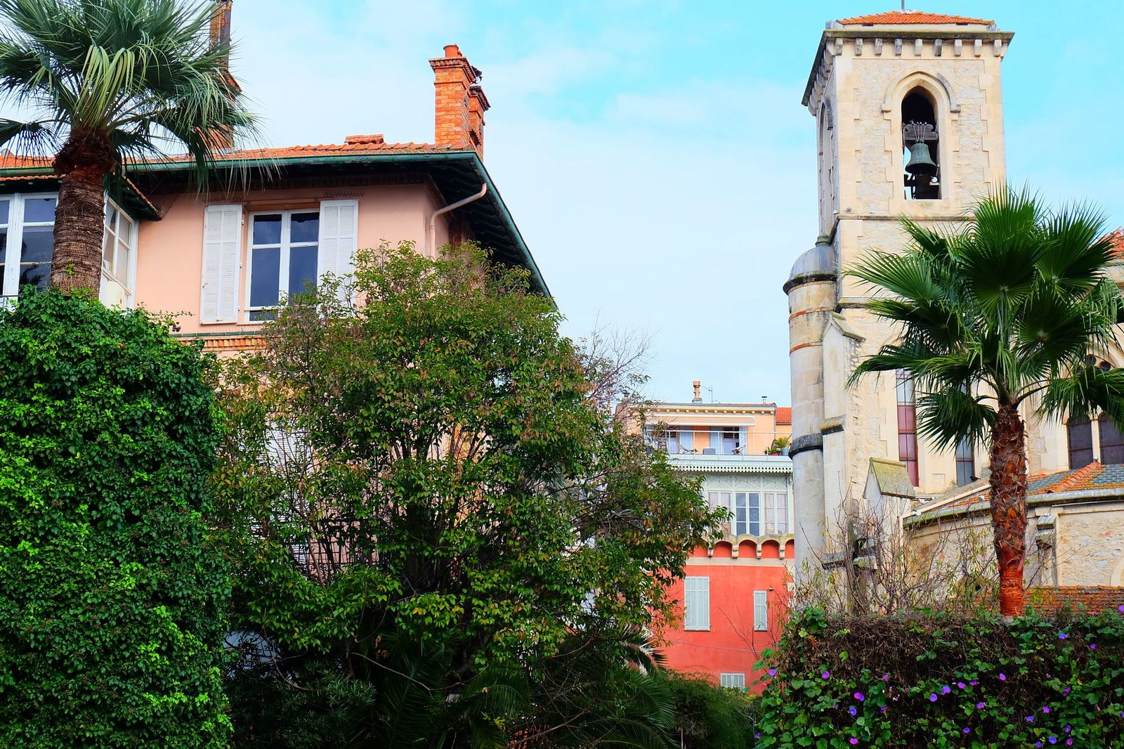 Le Cannet: a church bell tower above pastel houses and palm trees under a blue sky