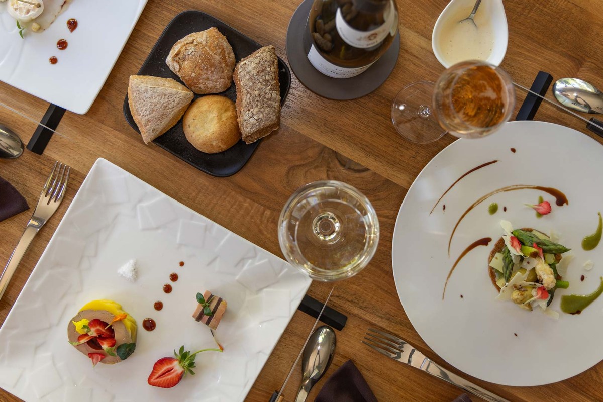 Overhead view of a laid table with multiple plated dishes, bread, and wine glasses