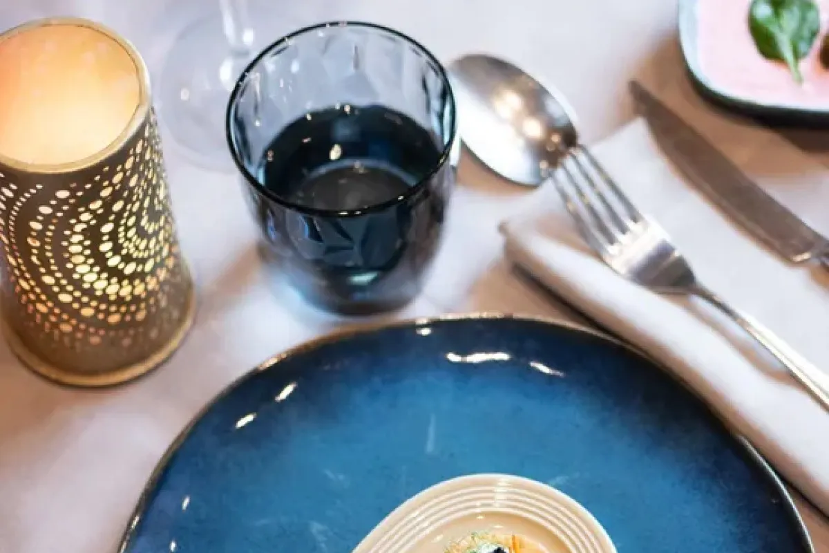 Elegant table setting with blue plate, candle lantern, wine glass and cutlery on white tablecloth