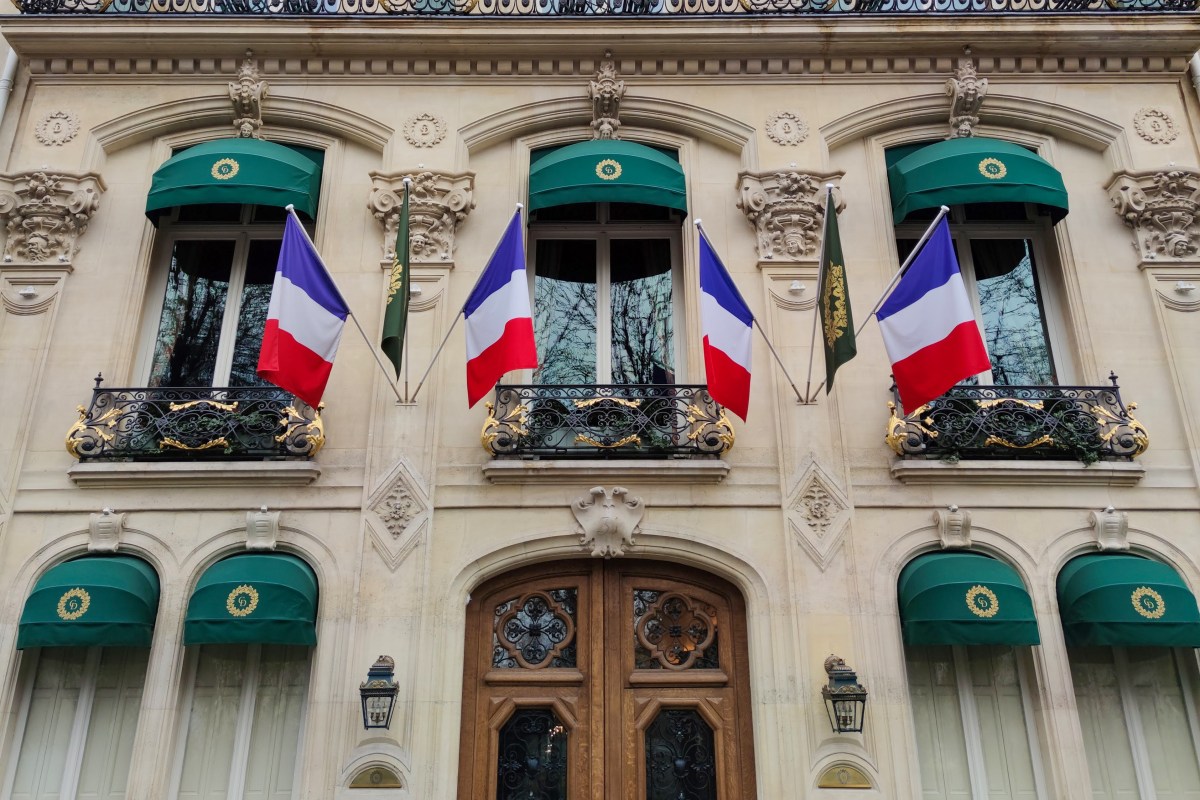 Facade of Le Clarence with green awnings, gold balconies, and French flags, close view with entrance door