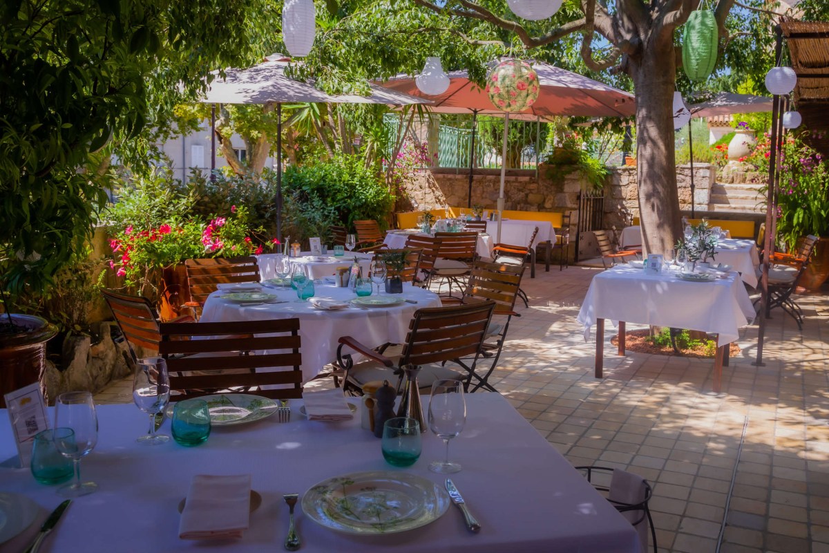 Sunlit outdoor terrace with white-clothed tables, lanterns, umbrellas and greenery at Le Clos Saint-Pierre